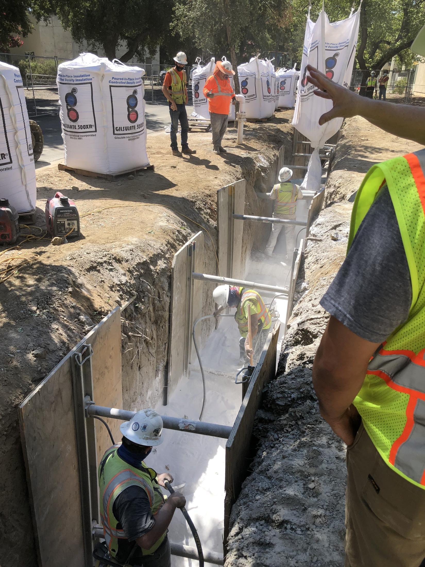 A construction crew installs Gilsulate in a hot water pipe trench
