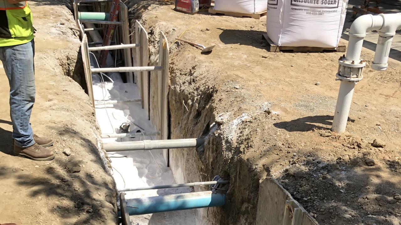 A trench with pipes partially covered by Gilsulate, a white powdery substance