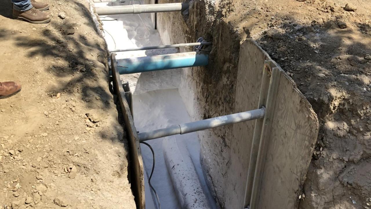 A trench with pipes partially covered by Gilsulate, a white powdery substance